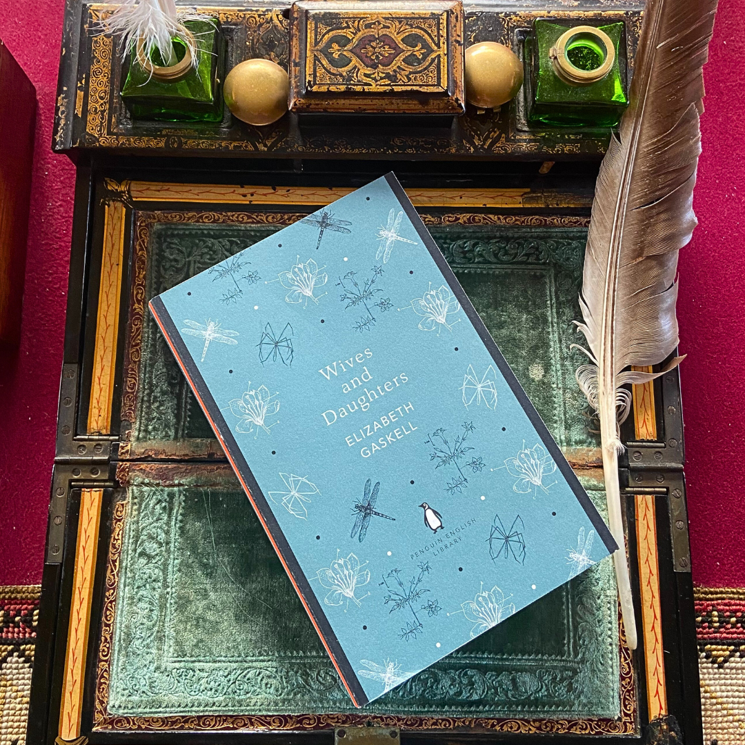 A copy of Wives and Daughters by Elizabeth Gaskell with a blue cover, on a green Victorian writing slope.