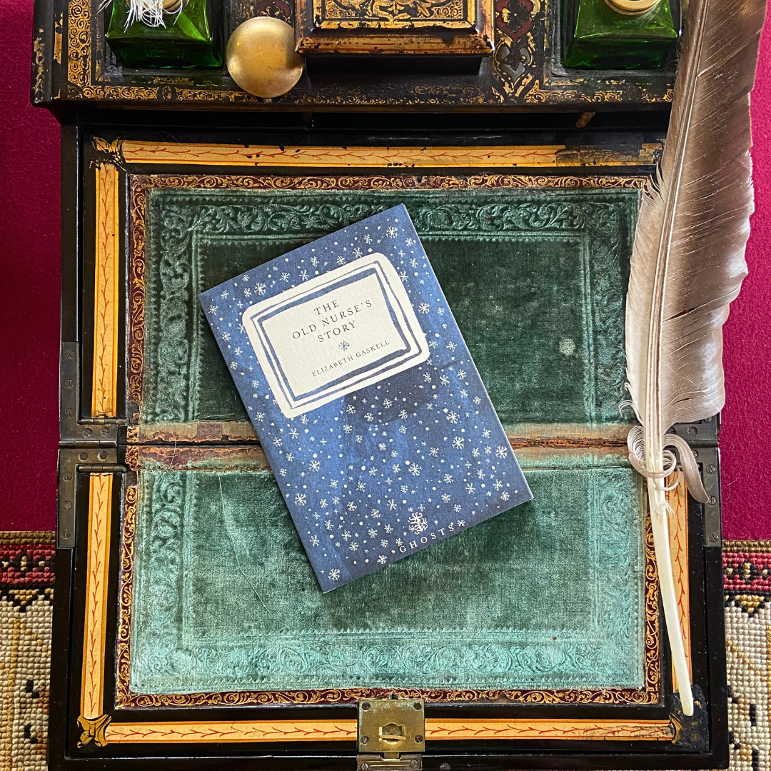 A copy of the Elizabeth Gaskell book The Old Nurse's Story, with a blue and white cover on a green velvet writing slope.